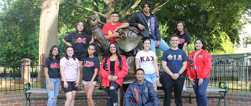 Multicultural Greek Council members pose in front of a bronze Cocky statue.