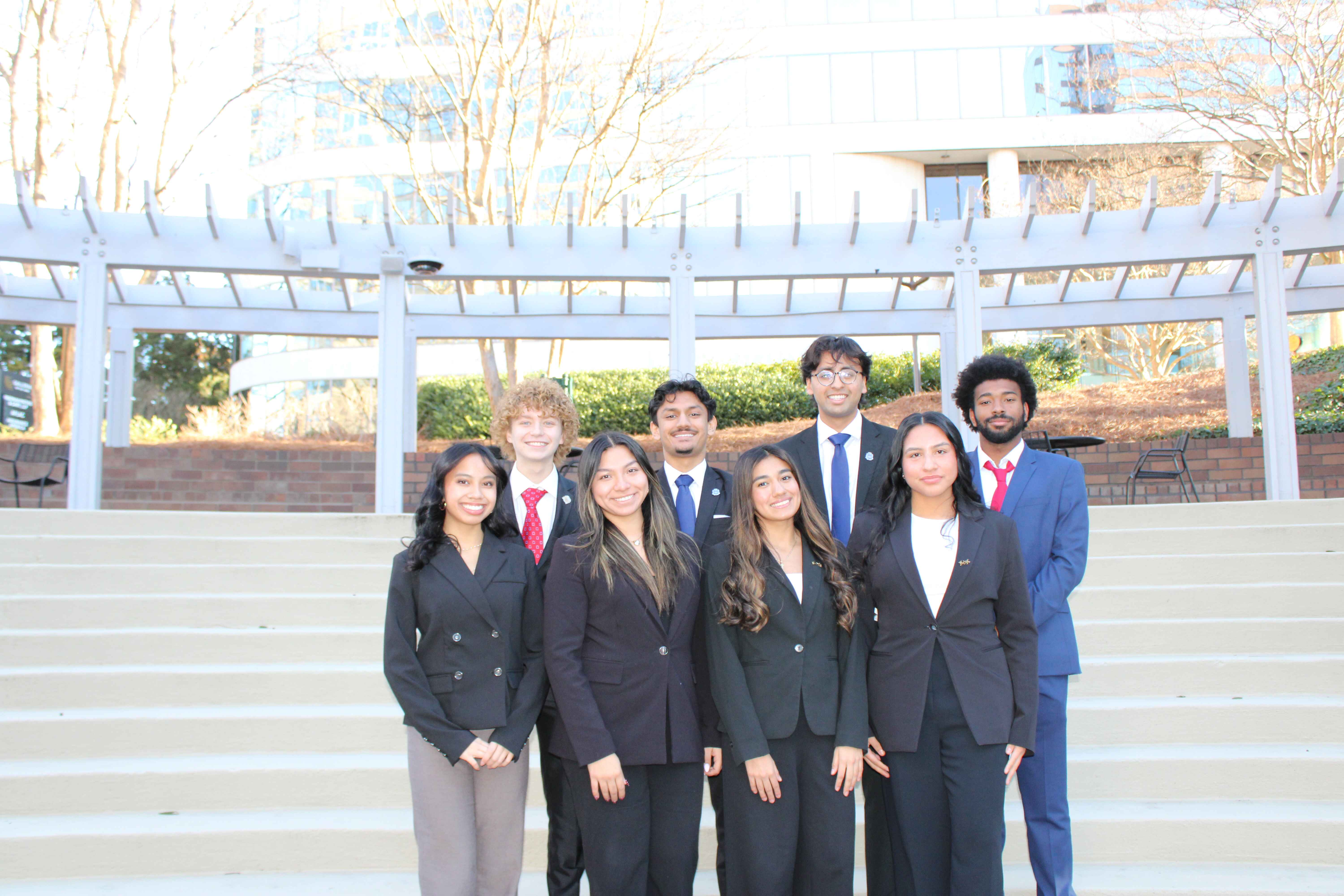 Multicultural Greek Council members pose in front of a bronze Cocky statue.