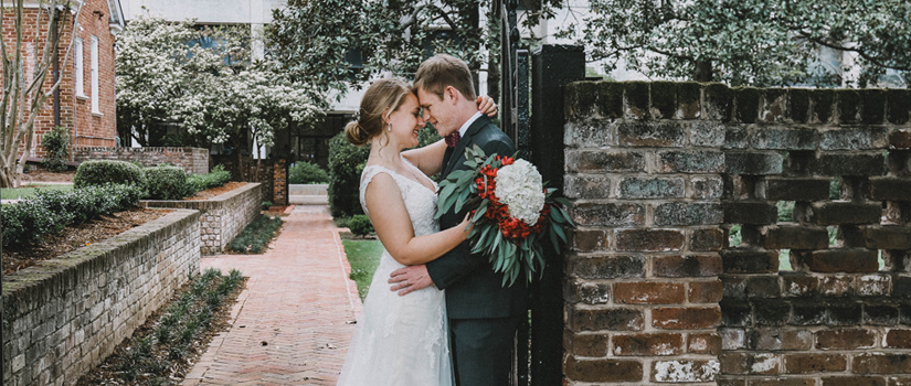 Bride and groom leaning against the brick gates of the garden