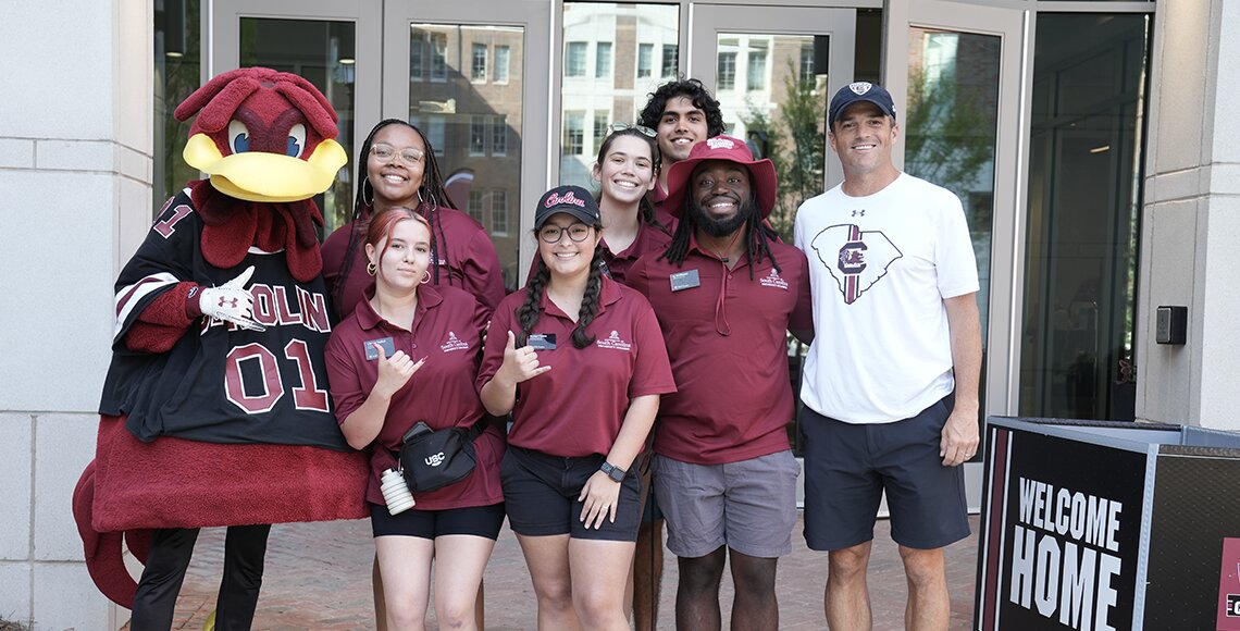 Students and staff standing outside of Campus Village 2 with the football Coach Beamer and USC mascot Cocky
