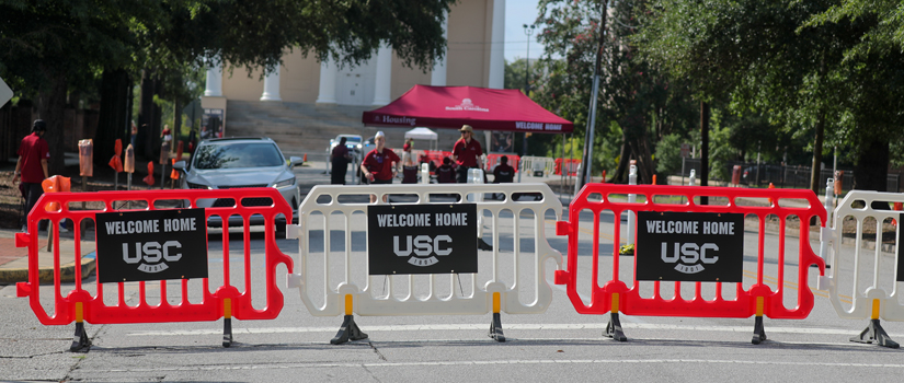 Red and white barriers with black welcome home signs are in the foreground with move in activities taking place in the background