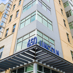 A photo looking upward at the 650 Lincoln building. Blue letters spelling "650 Lincoln" are on the corner of a metal awning with windows lining the blue and tan brick. 