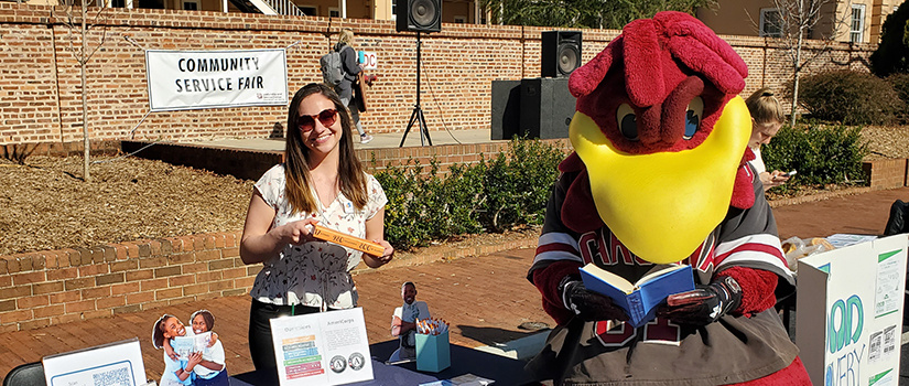 student poses next to UofSC mascot cocky reading a book.