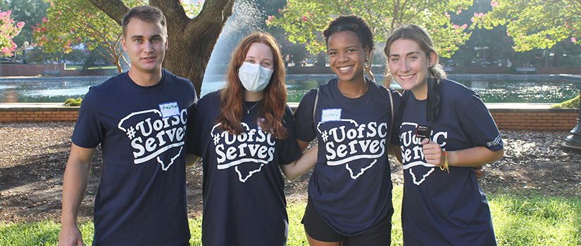Group of four students wearing a #UofSCServes t-shirt on Davis Field.  