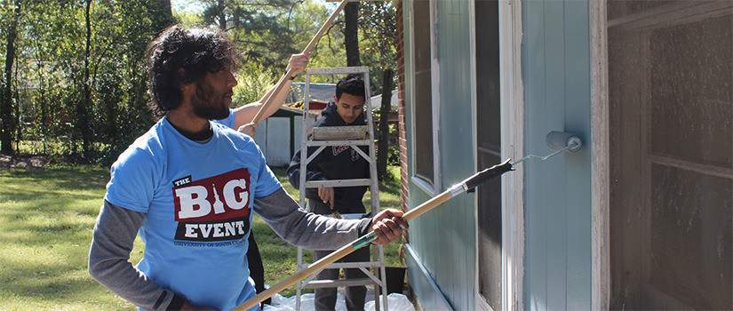 A student painting a house during The Big Event