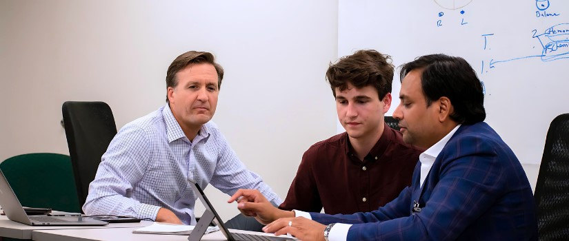 A student and two professionals sitting at a conference table around a computer