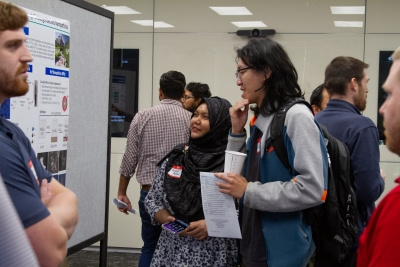 One man is presenting a poster as two event attendees look and discuss. 