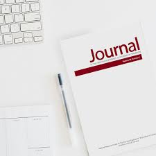 A white laptop, black ink pen, and a copy of The Journal placed together on top of a white desk