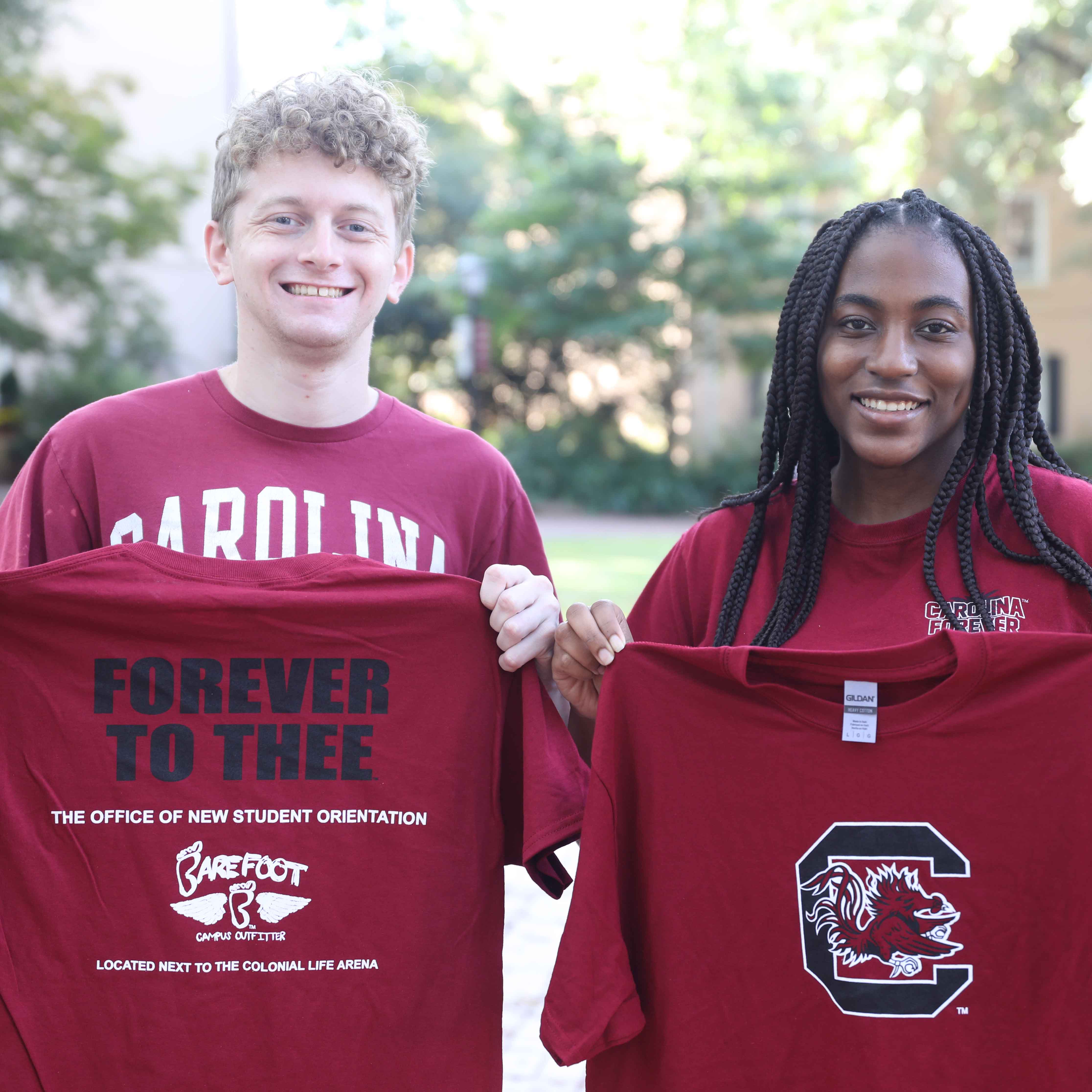 two students holding up shirts they received at new student orientation