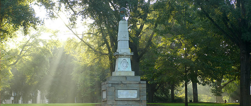 Sunlight filters down through the trees on a monument at the center of the horseshoe