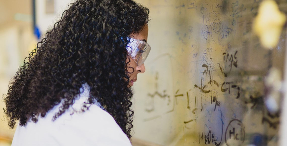 Latina student working on equations at a dry-erase board