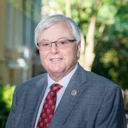 Portrait photo of USC President Michael Amiridis wearing a grey suit with a garnet tie.