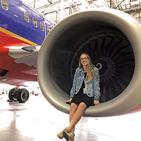 Megan Gallagher sits inside the front of a turbine engine on the wing of a red, blue and yellow Southwest airplane, which is parked in a hangar