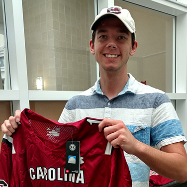 A male student holds a Carolina jersey and smiles