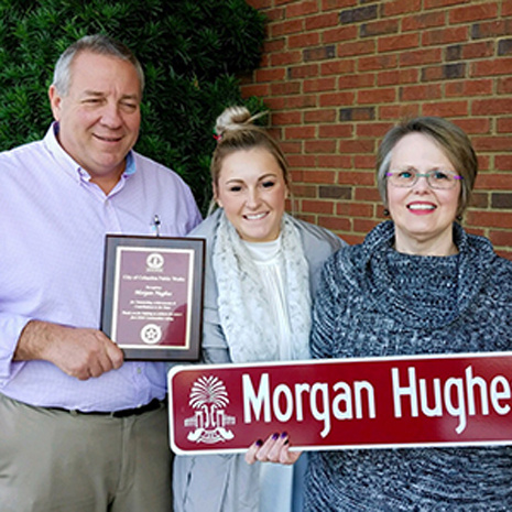 Morgan Hughes with two community members receiving "Morgan Hughes Street" sign and an award for her hard work