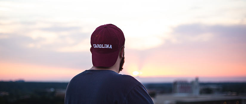 student wearing Carolina hat staring off into the sunset over Columbia from parking garage