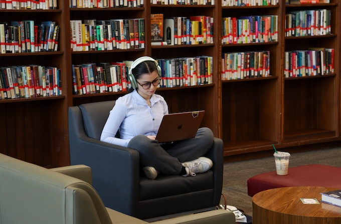 Girl sitting in library chair looking at laptop.