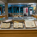 View of several display cases in the Irvin Department of Rare Books and Special Collections gallery, inside the Hollings Library. Three open books are displayed in the nearest case.