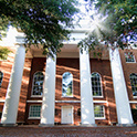 Exterior view of the front of the South Caroliniana Library. The low angle shows sunlight streaming through trees onto the red brick building and four white columns.