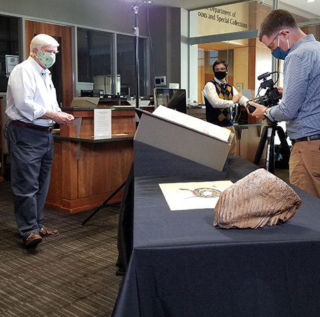 Rudy Mancke, Michael Weisenburg and a videographer on a video set with books and a giant fossilized mammoth tooth
