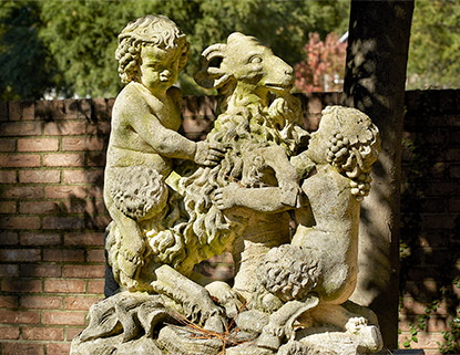 Stone statue of fauns and other mythical creatures in front of a brick wall.