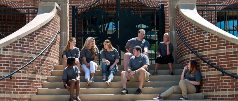 Group of students sits outside on the steps in front of the Alumni Center