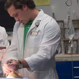 Male lab student in white lab coat practicing a medical treatment on a simulation mannequin
