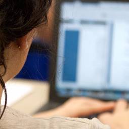 Close-up of the back of a student's head and right shoulder as she rests her hands on the keyboard of a laptop computer and looks at a document on its screen