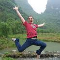 Student on study-abroad trip leaps joyfully outdoors in front of mountains and stream