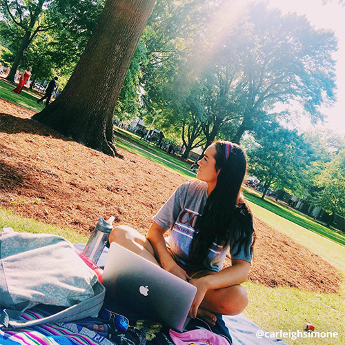 Female student sits on a blanket studying on the Horseshoe, laptop open.