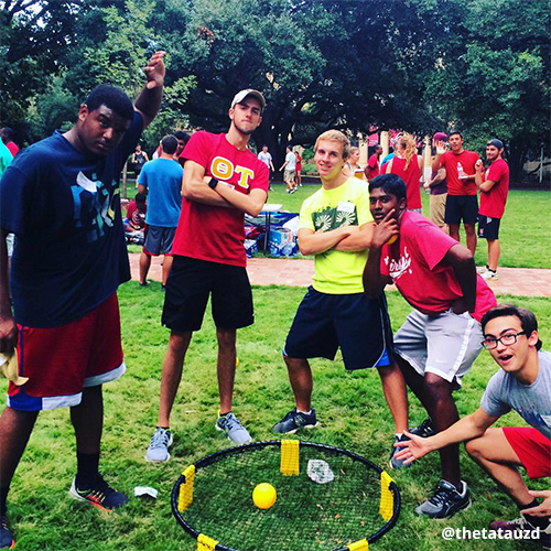 Five male students pause Spikeball game to pose playfully around trampoline and ball.