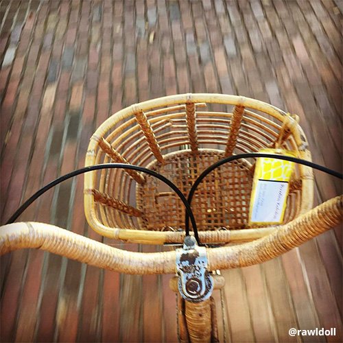 Wooden bike basket attached to handlebars of moving bike as red bricks speed below.