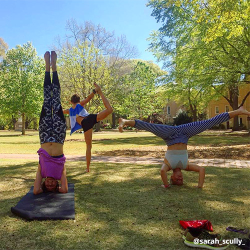 Female students flaunt yoga poses and headstands while exercising on Horseshoe grass.