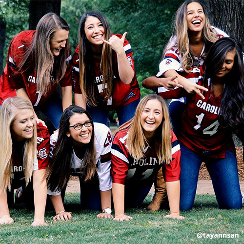 Group of smiling female students wearing Gamecock football jerseys pose in human pyramid.
