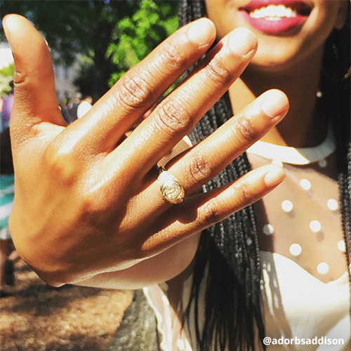 Female student in white dress proudly holds hand in front of camera displaying new class ring.