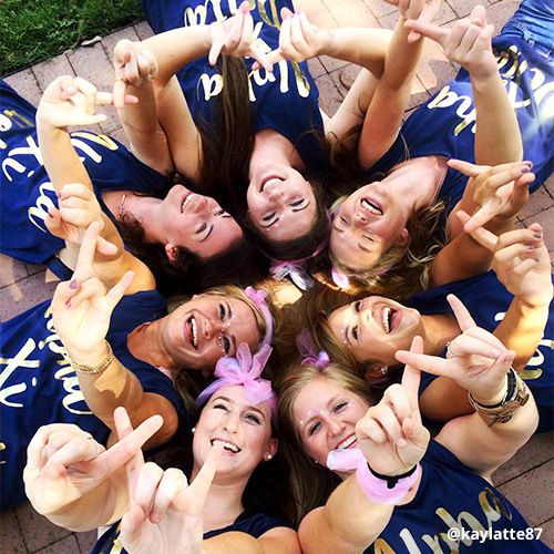 Alpha Xi Delta sorority sisters strike Bid Day pose, laying on brick sidewalk with heads in center.