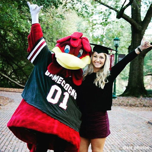 Female student wears graduation cap while posing with Cocky on Horseshoe.