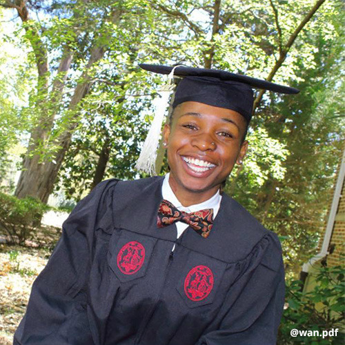 Student wearing bow tie, graduation cap and gown, flashes a huge smile.