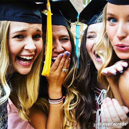 Four female students laugh and blow kisses at camera while posing in graduation caps.