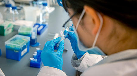 Looking over a researcher's shoulder pipetting into a small tube. 