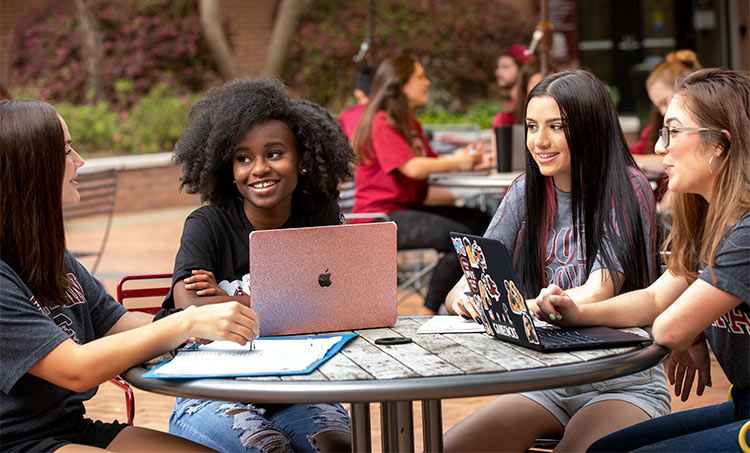 Students gathered at an outside table studying together with laptops and notebooks.