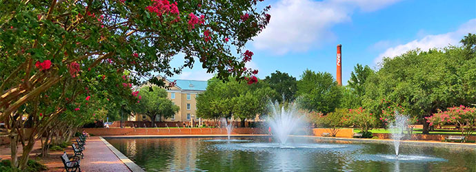 Three fountains in a reflecting pool surrounded by benches with a view of campus and the USC smokestack in the background.
