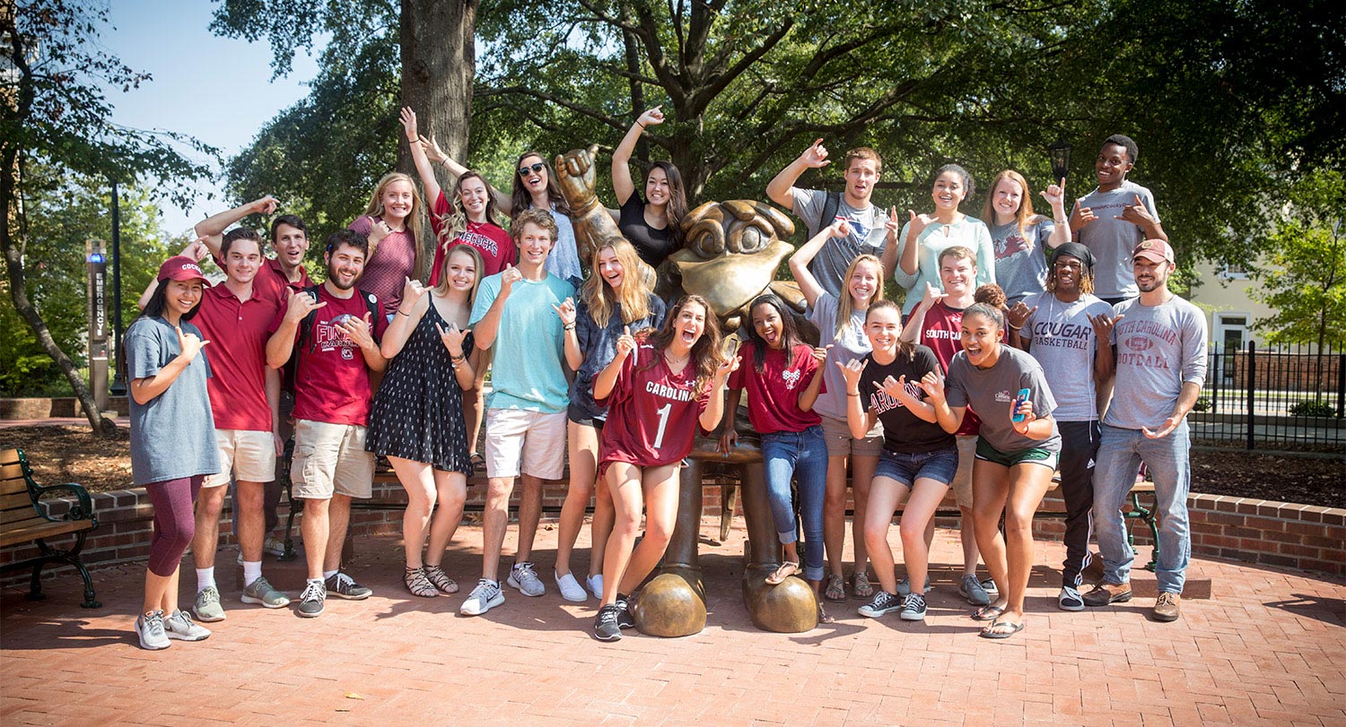 Large group of students gathered around the Cocky Statue smiling at the camera.