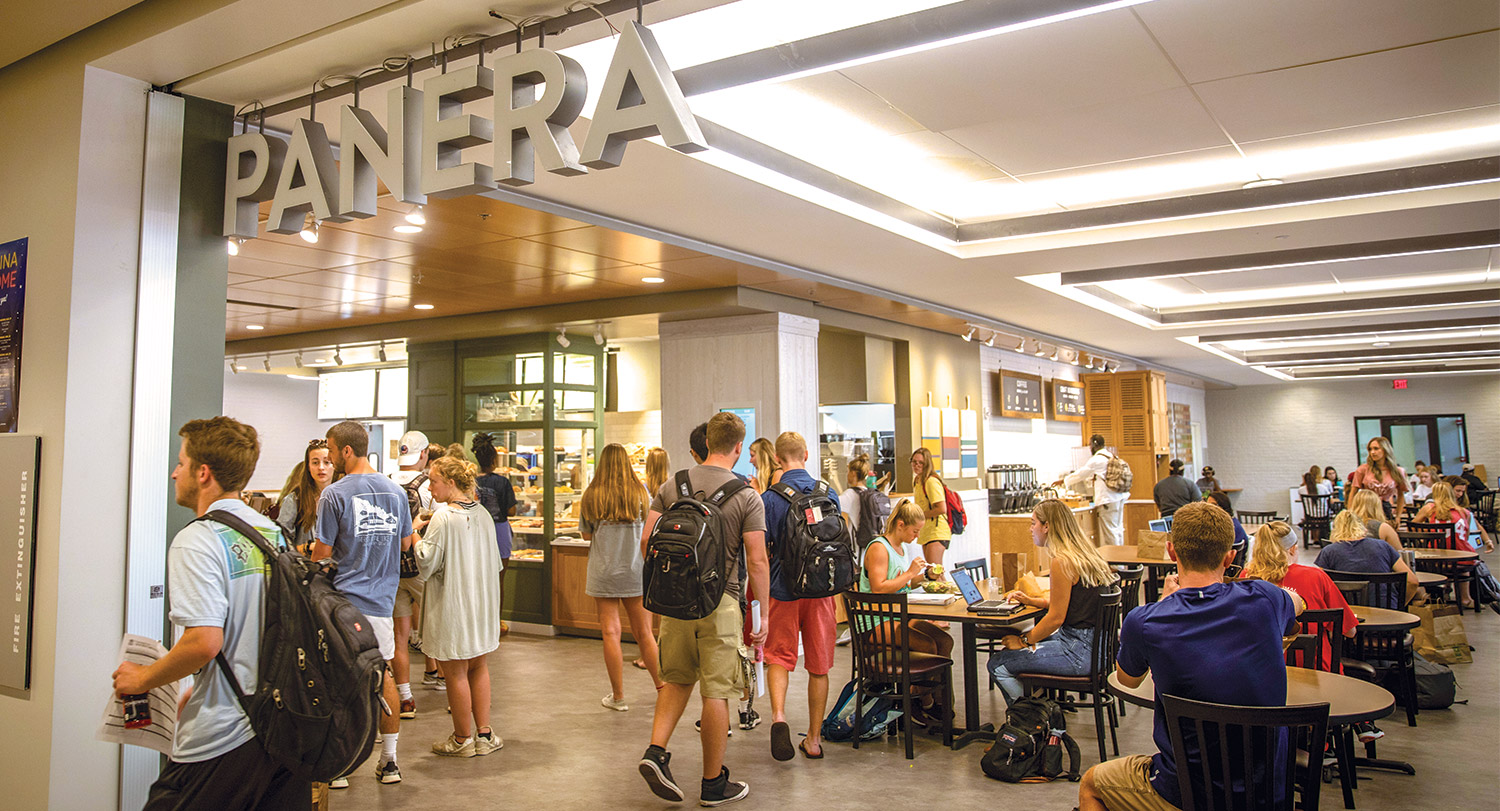 Students eating at tables in the Panera restaurant in the Russell House. 