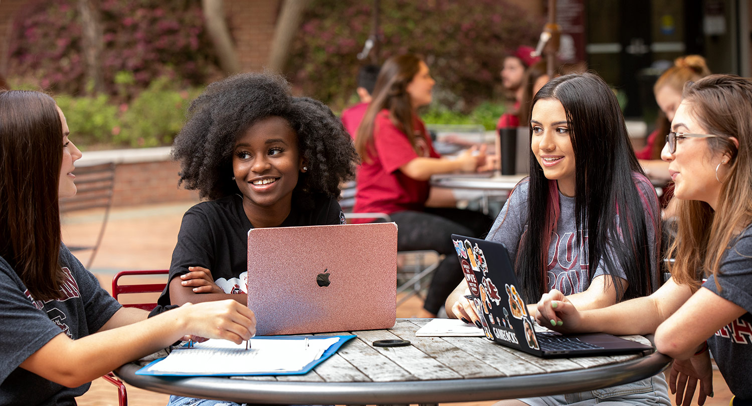 Students gathered at an outside table studying together with laptops and notebooks. 