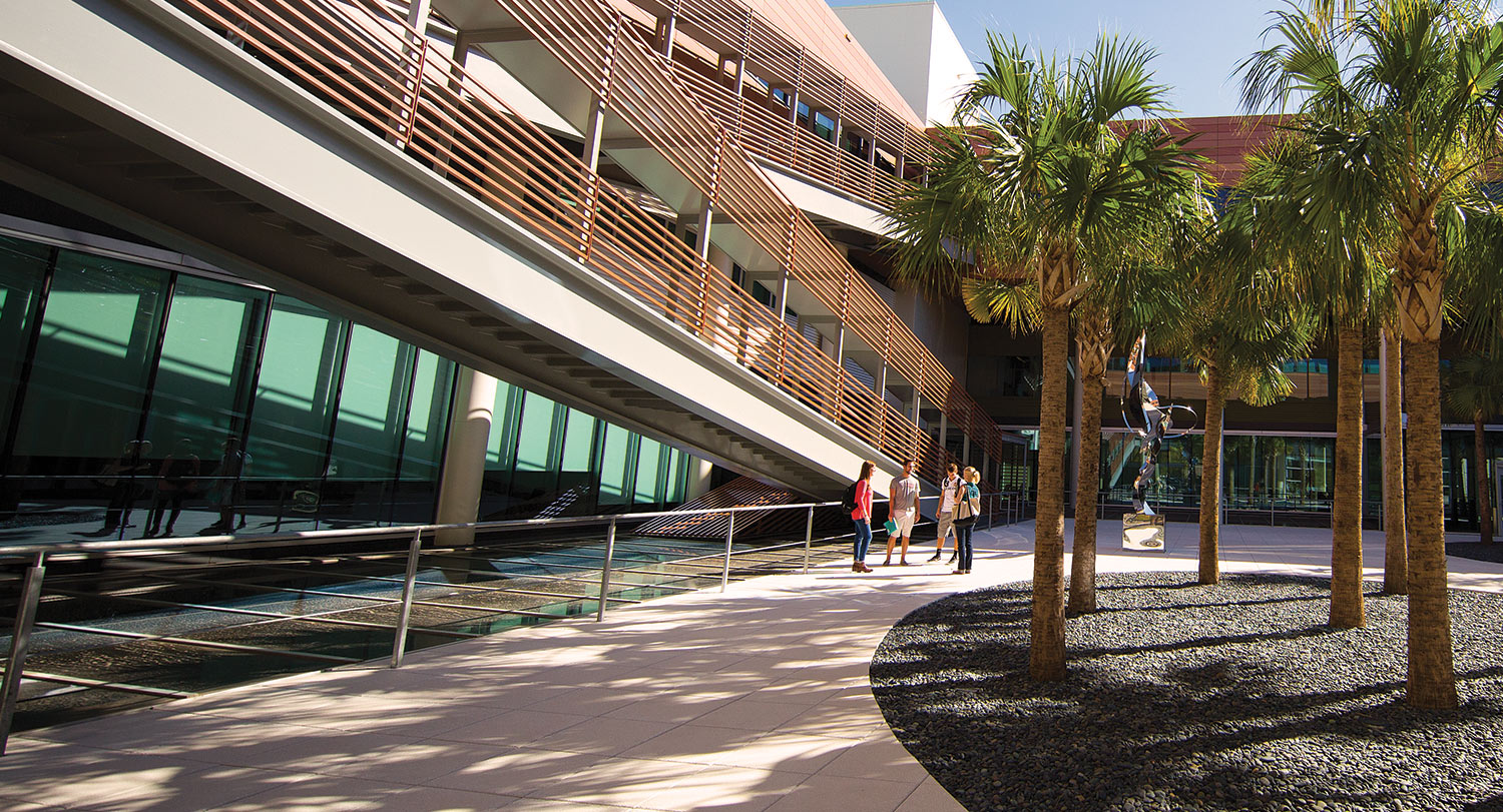 Four students gathered in the courtyard of the Darla Moore School of Business with stairs on the left and palmetto trees on the right.
