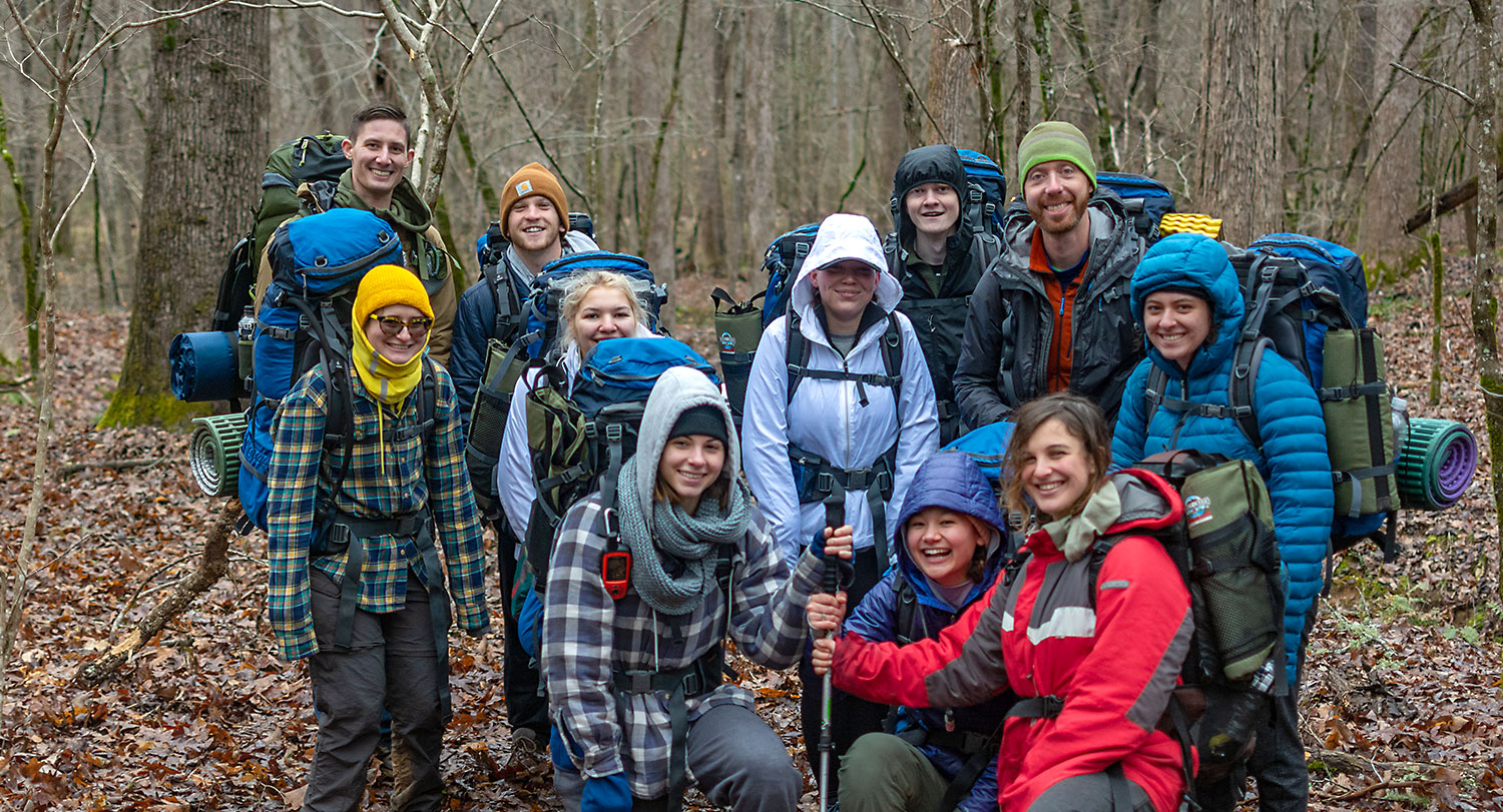 Group of students wearing hiking gear and backpacks in the woods on an Ourdoor Rec adventure trip. 