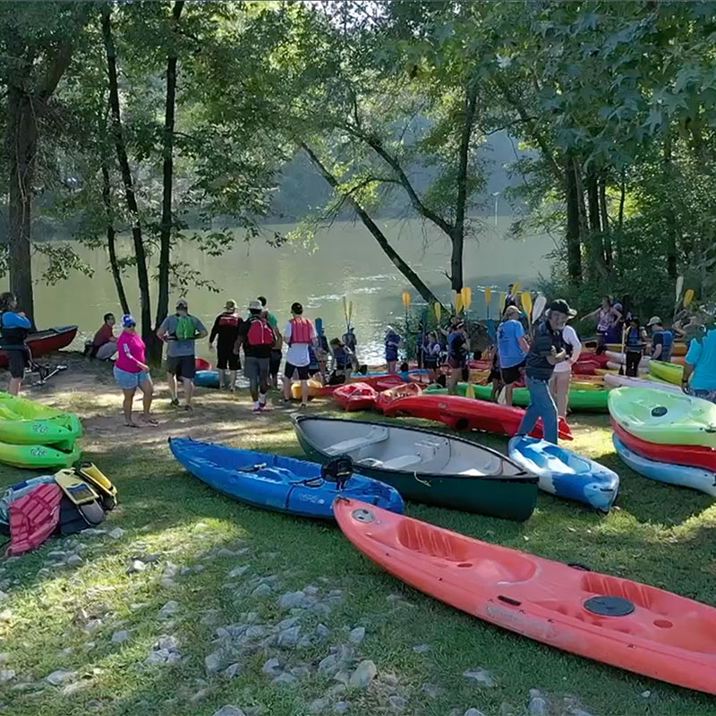 A group of students gathered on the riverbank with kayaks.
