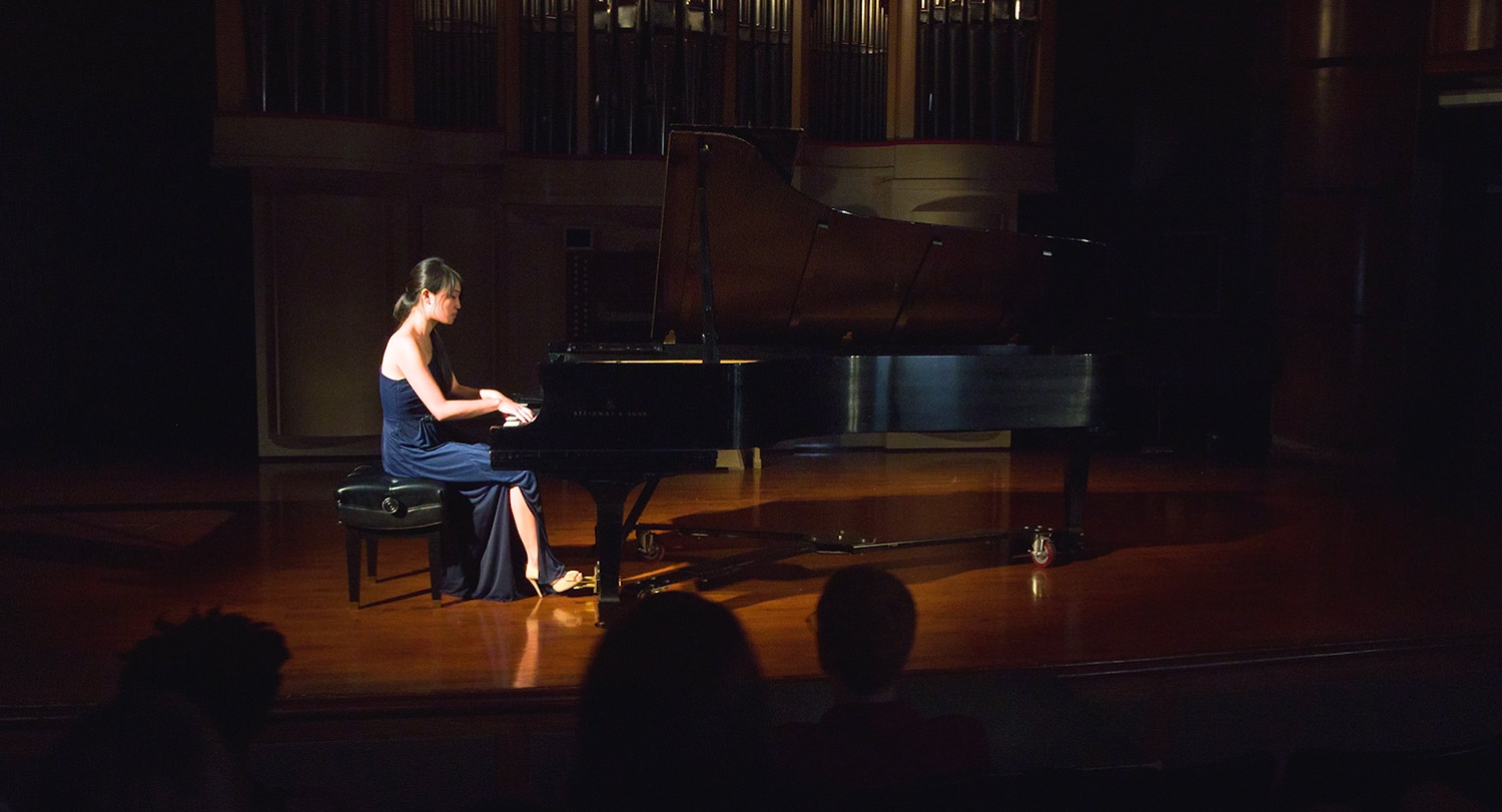Student playing a grand piano on a stage.
