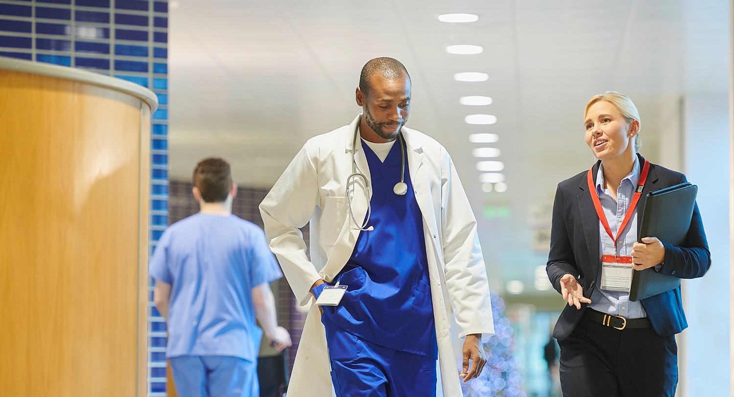 Person in a business suit walking and talking with a doctor in scrubs and a lab coat. 